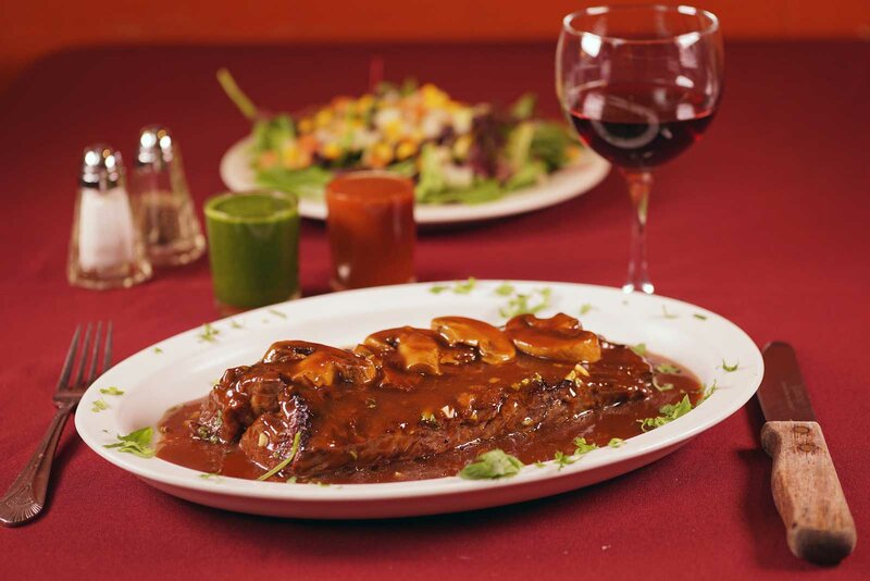 Steak entree topped with mushrooms with a glass of red wine